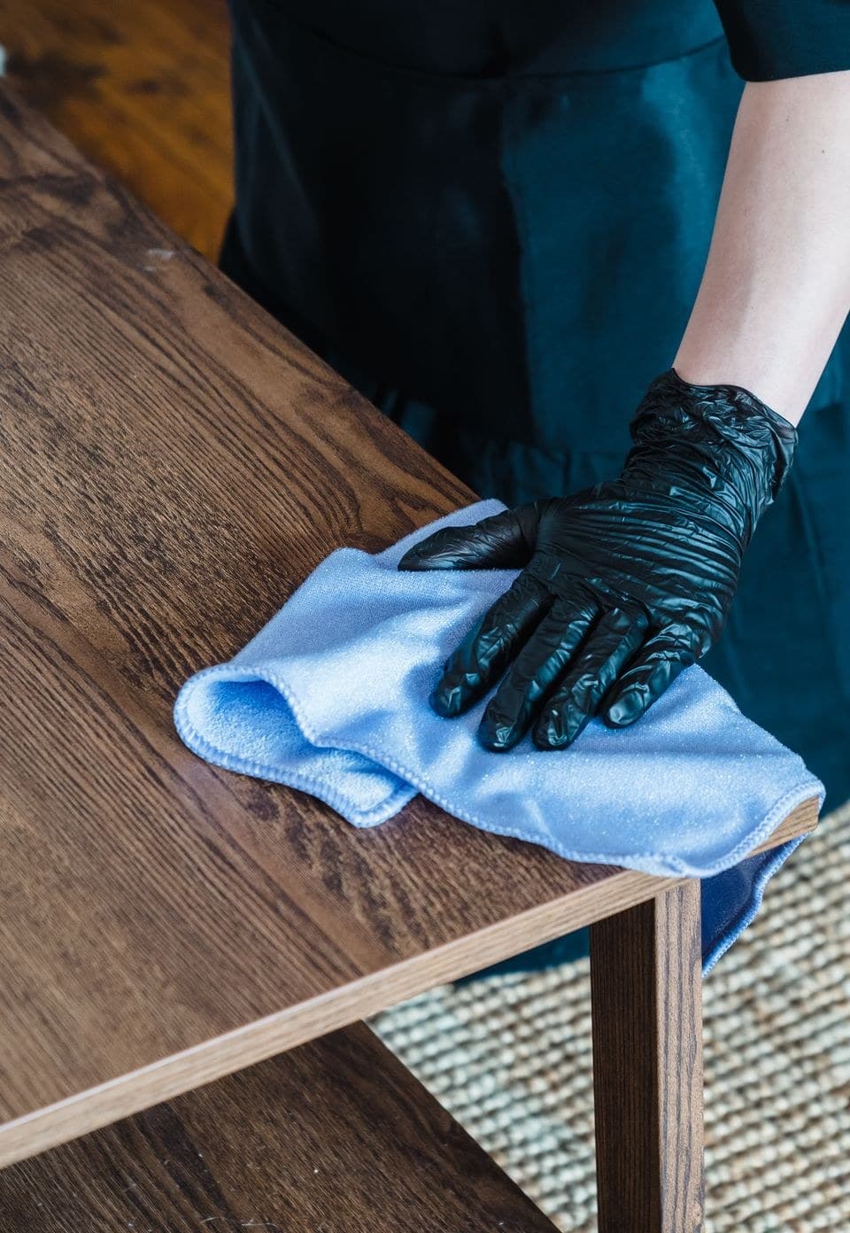 Main gantée essuyant une table en bois, blouse et tablier de travail
